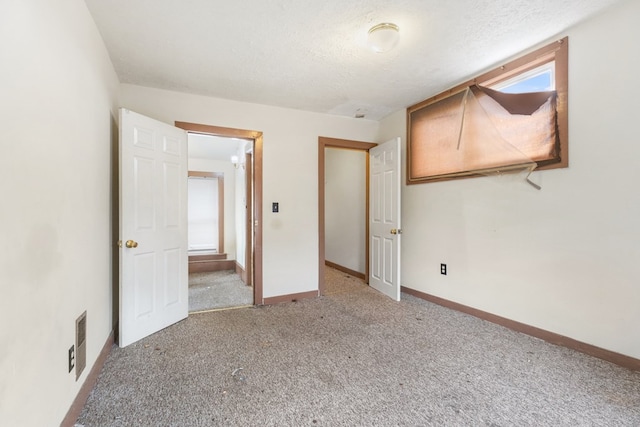 unfurnished bedroom with carpet floors, visible vents, a textured ceiling, and baseboards