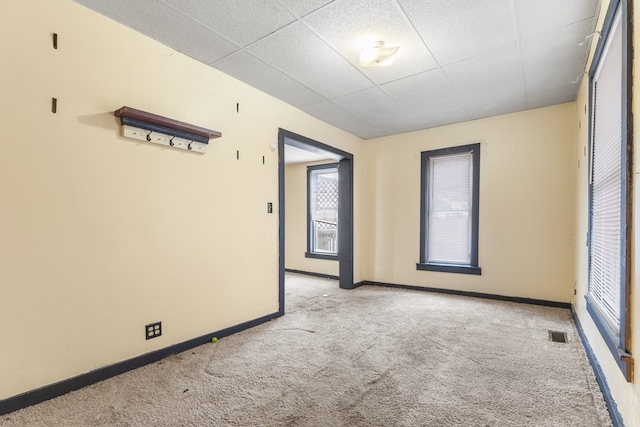 spare room featuring a paneled ceiling, light carpet, visible vents, and baseboards