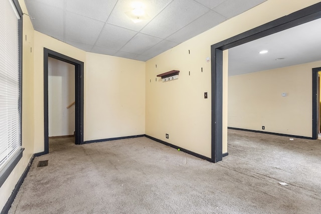 empty room with light carpet, baseboards, and a drop ceiling