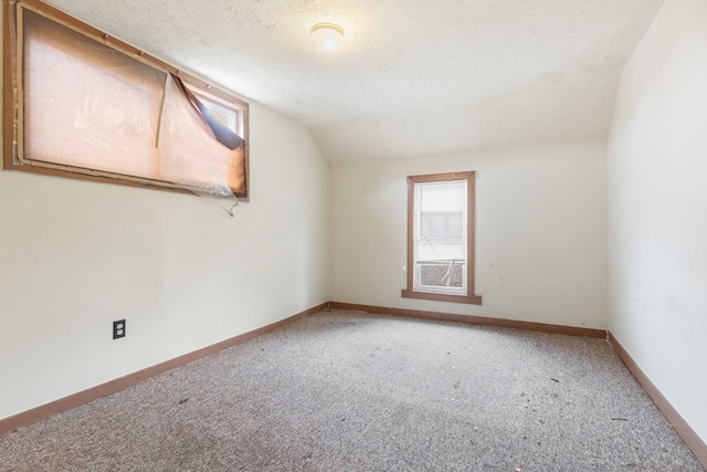 spare room with carpet flooring, vaulted ceiling, a textured ceiling, and baseboards