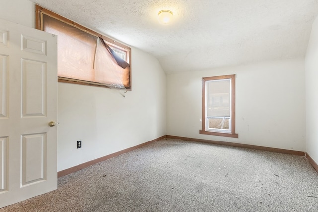 carpeted spare room with lofted ceiling, a textured ceiling, and baseboards