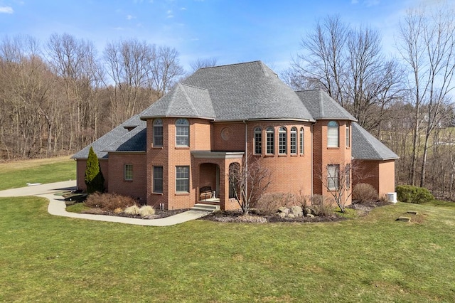 french country style house with roof with shingles, a front lawn, and brick siding