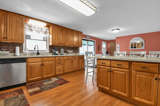 kitchen featuring stainless steel dishwasher, a sink, light countertops, brown cabinets, and light wood finished floors