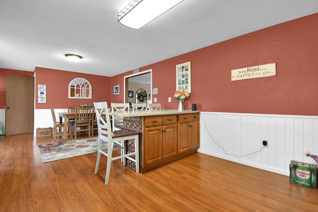 kitchen featuring a peninsula, light wood-style flooring, light countertops, a wainscoted wall, and brown cabinets