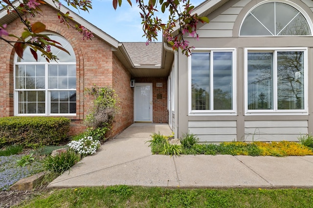 entrance to property featuring brick siding and a shingled roof