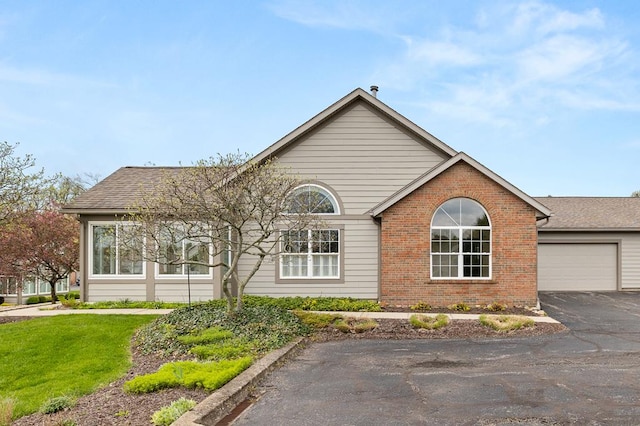 view of front of house featuring aphalt driveway, a front yard, brick siding, a shingled roof, and an attached garage