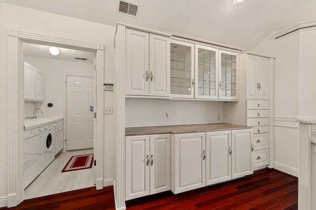 kitchen with visible vents, washing machine and dryer, white cabinets, dark wood-style floors, and glass insert cabinets