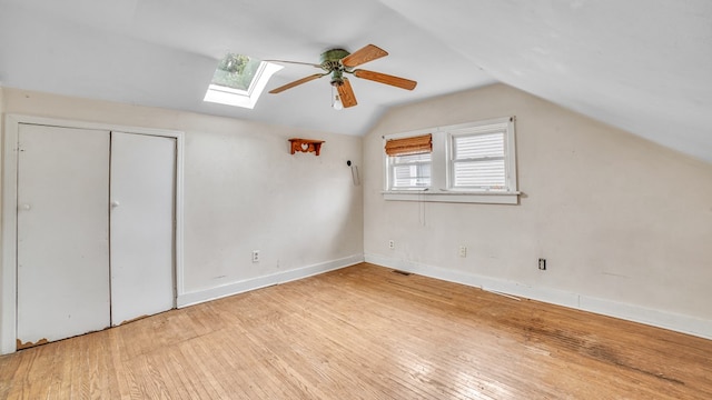additional living space featuring visible vents, baseboards, ceiling fan, vaulted ceiling with skylight, and hardwood / wood-style floors