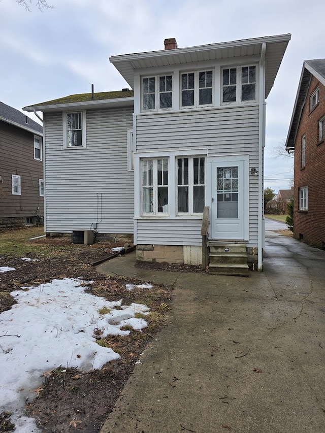 rear view of house featuring entry steps, central AC, and a chimney