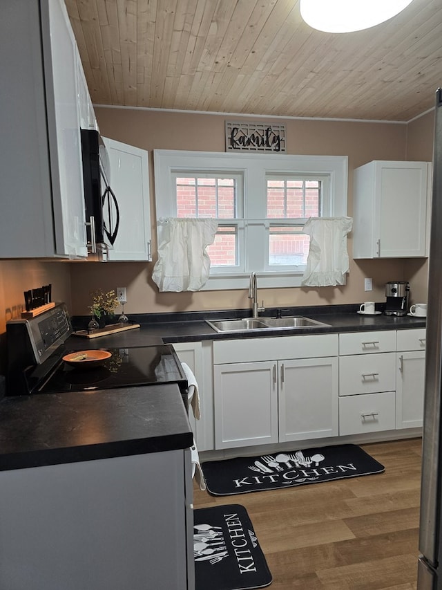 kitchen with black microwave, electric stove, dark countertops, white cabinetry, and a sink