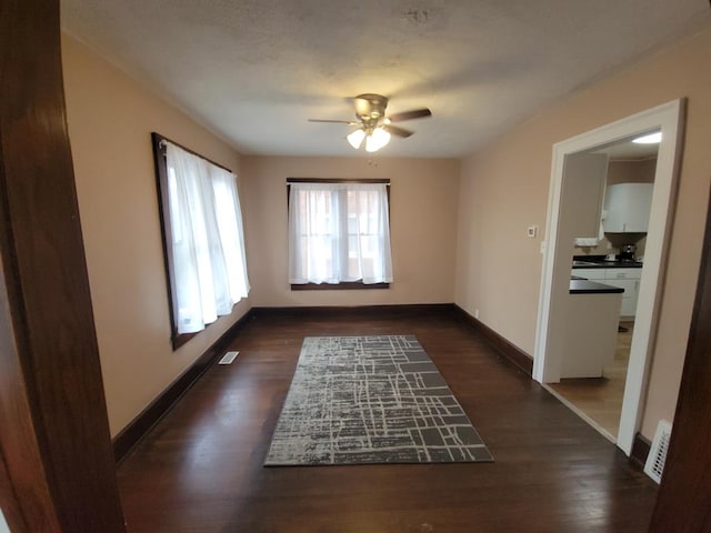 empty room featuring ceiling fan, visible vents, baseboards, and dark wood-type flooring