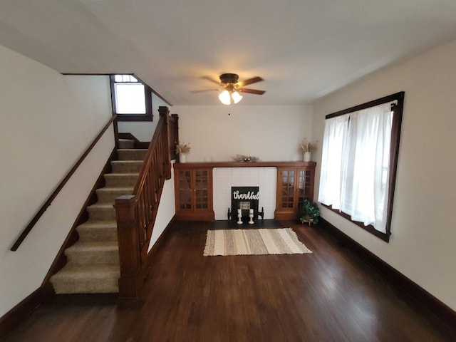 unfurnished living room featuring dark wood-style floors, a brick fireplace, stairs, and baseboards