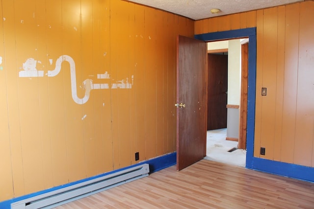 unfurnished room with a textured ceiling, a baseboard radiator, light hardwood / wood-style flooring, and wood walls