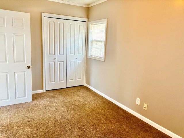 unfurnished bedroom featuring a closet, ornamental molding, baseboards, and carpet floors