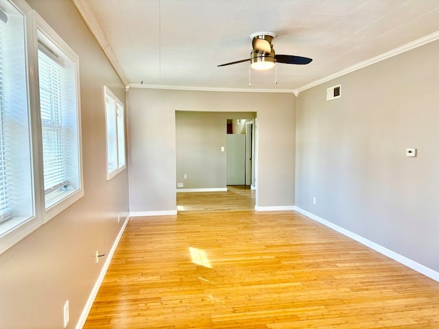 spare room featuring baseboards, visible vents, ceiling fan, light wood-style floors, and crown molding