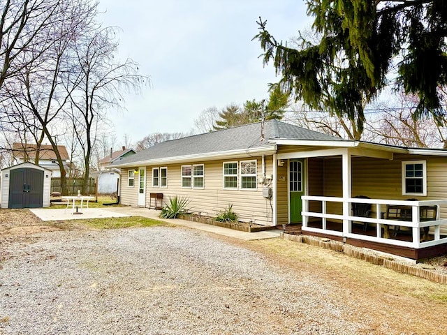 rear view of property featuring an outbuilding, driveway, roof with shingles, a storage unit, and a patio area