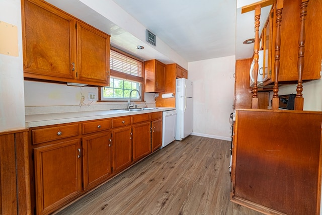 kitchen featuring light wood-style floors, a sink, brown cabinets, and white appliances