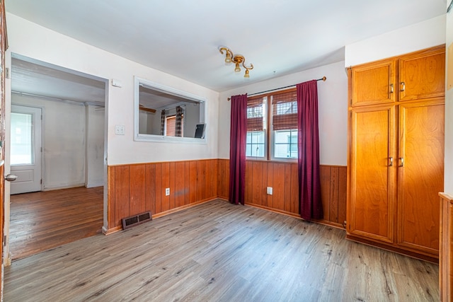 unfurnished dining area with visible vents, light wood-style flooring, wainscoting, and wooden walls