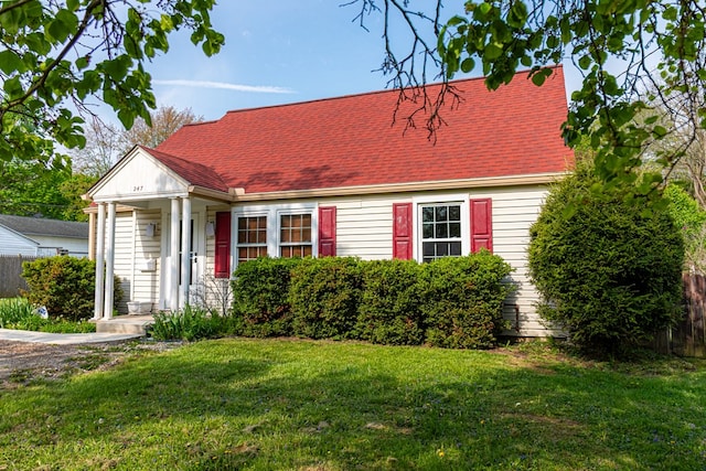 cape cod home with fence, a shingled roof, and a front lawn
