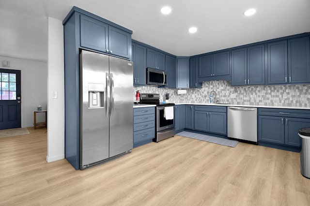 kitchen featuring appliances with stainless steel finishes, blue cabinetry, light wood-type flooring, and decorative backsplash