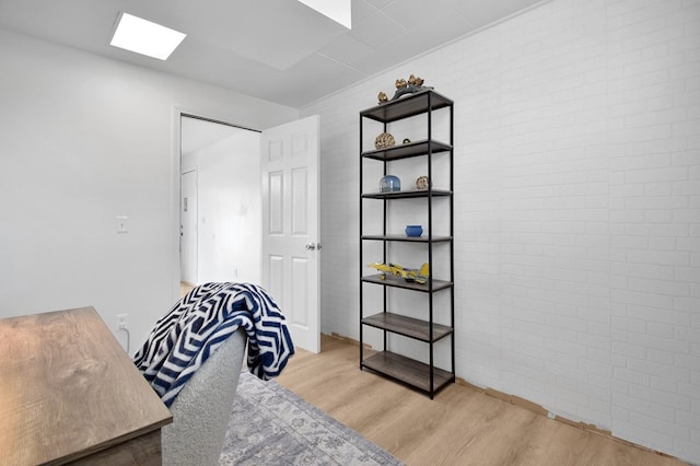 living area featuring brick wall, a skylight, and light hardwood / wood-style floors