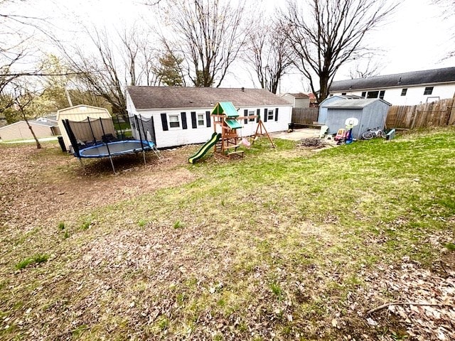 rear view of property featuring a playground, fence, a storage shed, a lawn, and a trampoline