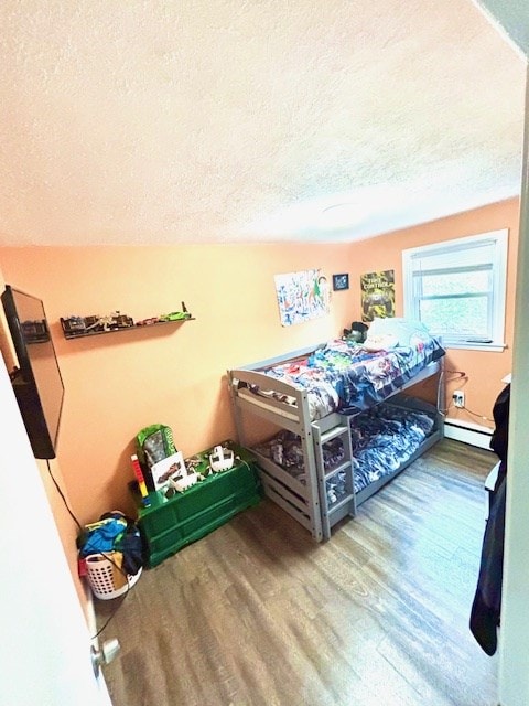 bedroom with a baseboard heating unit, wood finished floors, and a textured ceiling