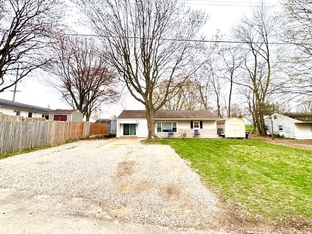 rear view of property with a storage shed, driveway, fence, a lawn, and an outdoor structure
