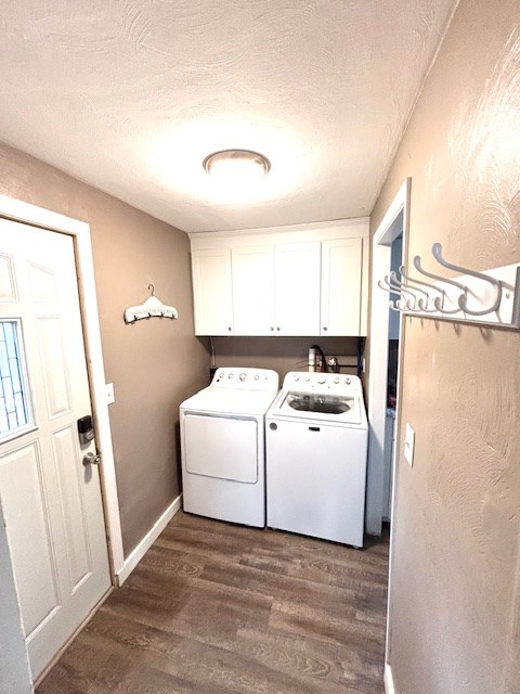 washroom with a textured ceiling, washer and dryer, cabinet space, baseboards, and dark wood-type flooring
