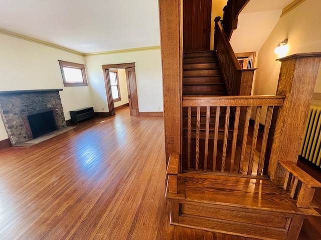 stairway with baseboards, wood finished floors, a stone fireplace, and ornamental molding