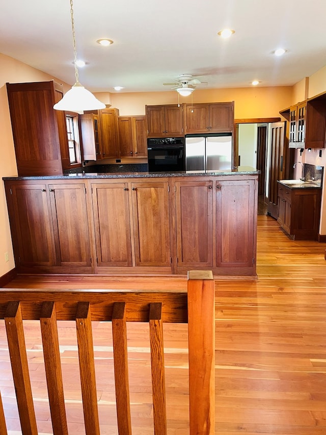 kitchen with oven, built in fridge, a ceiling fan, light wood-style flooring, and hanging light fixtures