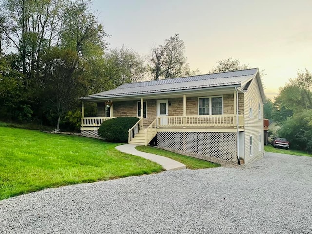 view of front of home featuring covered porch, a yard, metal roof, and gravel driveway
