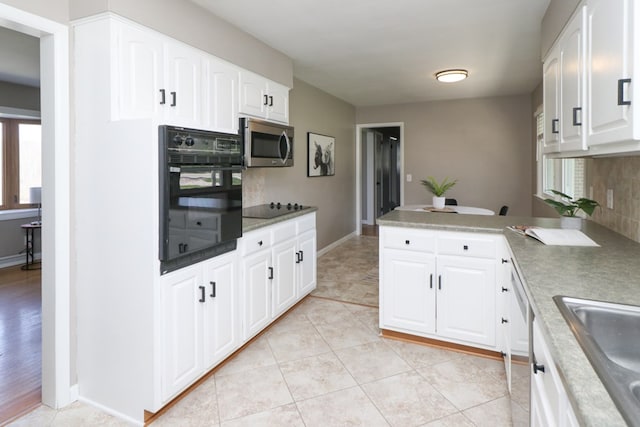 kitchen featuring white cabinets, a peninsula, a sink, tasteful backsplash, and black appliances