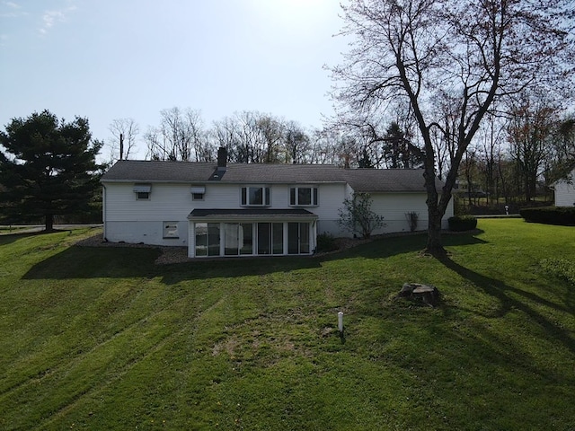 rear view of house with a lawn, a chimney, and a sunroom