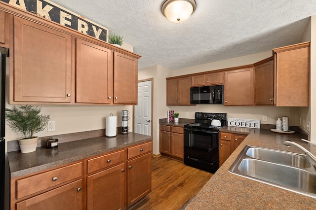 kitchen featuring a sink, dark countertops, black appliances, and dark wood-style floors