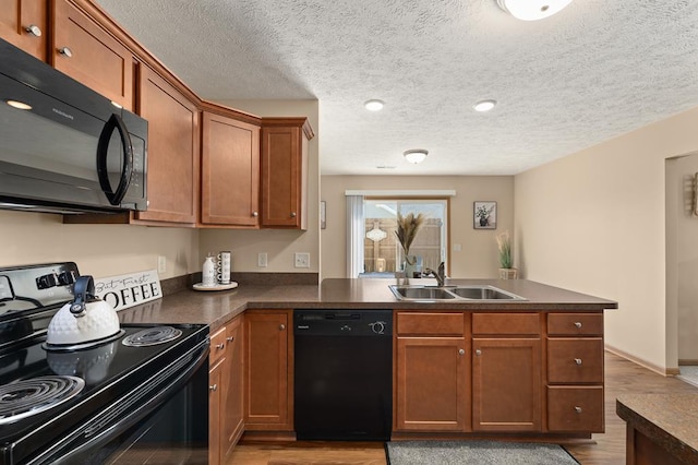 kitchen with dark countertops, brown cabinets, a sink, black appliances, and a peninsula