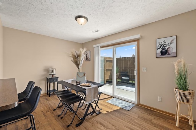 dining area featuring light wood-style floors, baseboards, a textured ceiling, and visible vents