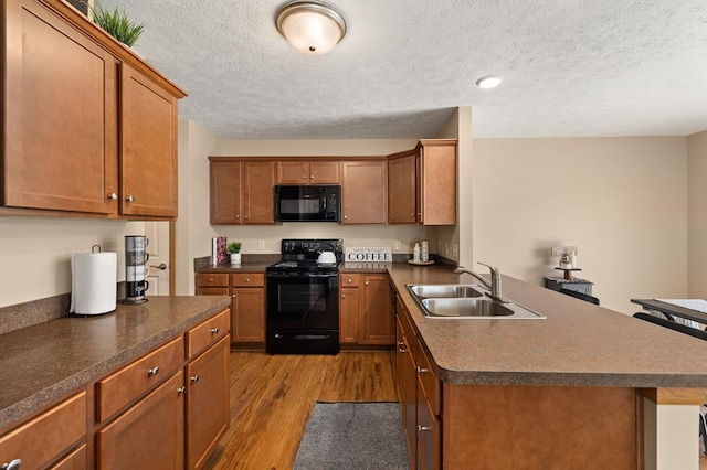 kitchen featuring wood finished floors, dark countertops, a textured ceiling, a sink, and black appliances