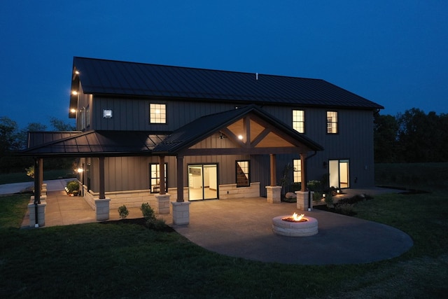 back of house at night featuring board and batten siding, a fire pit, a patio, metal roof, and a standing seam roof