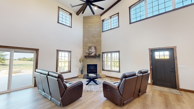 living room featuring ceiling fan, a large fireplace, high vaulted ceiling, and light wood-type flooring