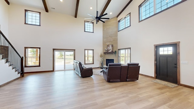 living room with a towering ceiling, a fireplace, ceiling fan, light hardwood / wood-style flooring, and beamed ceiling