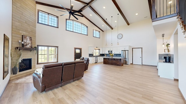 living room featuring a large fireplace, beamed ceiling, light hardwood / wood-style floors, and a high ceiling