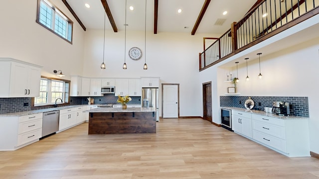 kitchen featuring beamed ceiling, appliances with stainless steel finishes, a towering ceiling, and decorative light fixtures