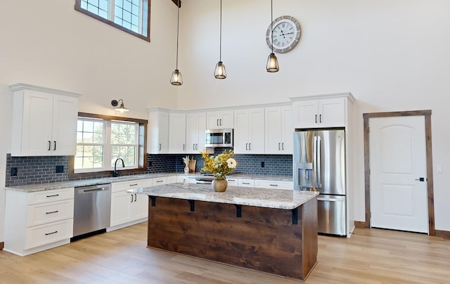 kitchen with appliances with stainless steel finishes, a center island, hanging light fixtures, and a high ceiling