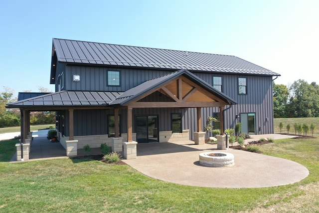 back of property with a fire pit, a patio area, and a lawn