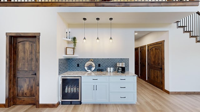 kitchen featuring light stone countertops, beverage cooler, hanging light fixtures, white cabinets, and light wood-type flooring