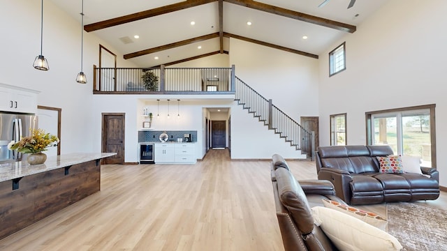 living room featuring beamed ceiling, light hardwood / wood-style floors, a towering ceiling, and wine cooler