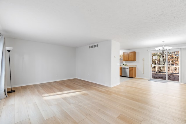 unfurnished living room featuring light wood-type flooring, a textured ceiling, and a notable chandelier