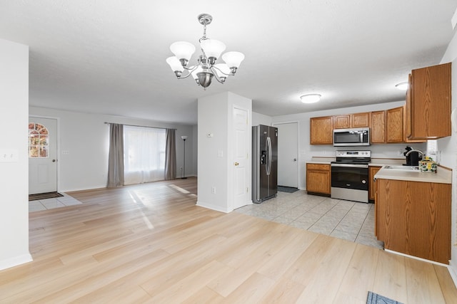 kitchen with sink, a textured ceiling, light wood-type flooring, appliances with stainless steel finishes, and pendant lighting