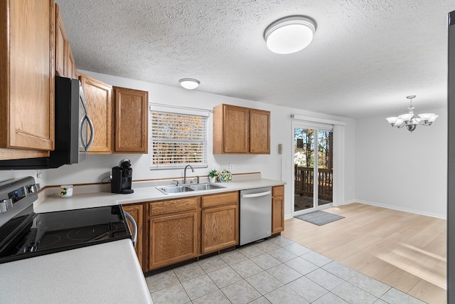 kitchen with appliances with stainless steel finishes, decorative light fixtures, sink, a textured ceiling, and light wood-type flooring